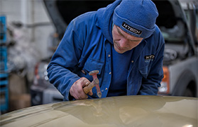 Car bodywork specialist carefully beating out dent from bonnet