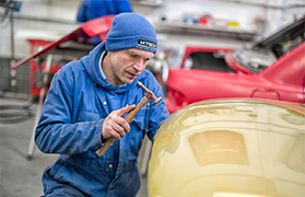 Car bodywork specialist carefully dressing dent in peugeot bonnet
