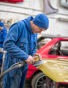Car bodywork specialist sanding back bonnet dent